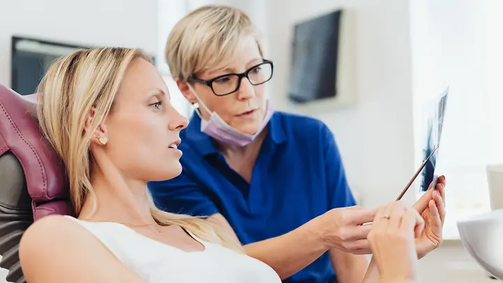 Zahnärztin erklärt Patientin die Kosten für Zahnfüllungen.